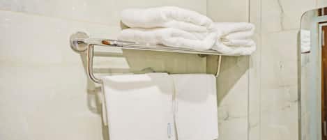 A bathroom with a marble wall, a towel rack with folded towels, and a hand dryer.