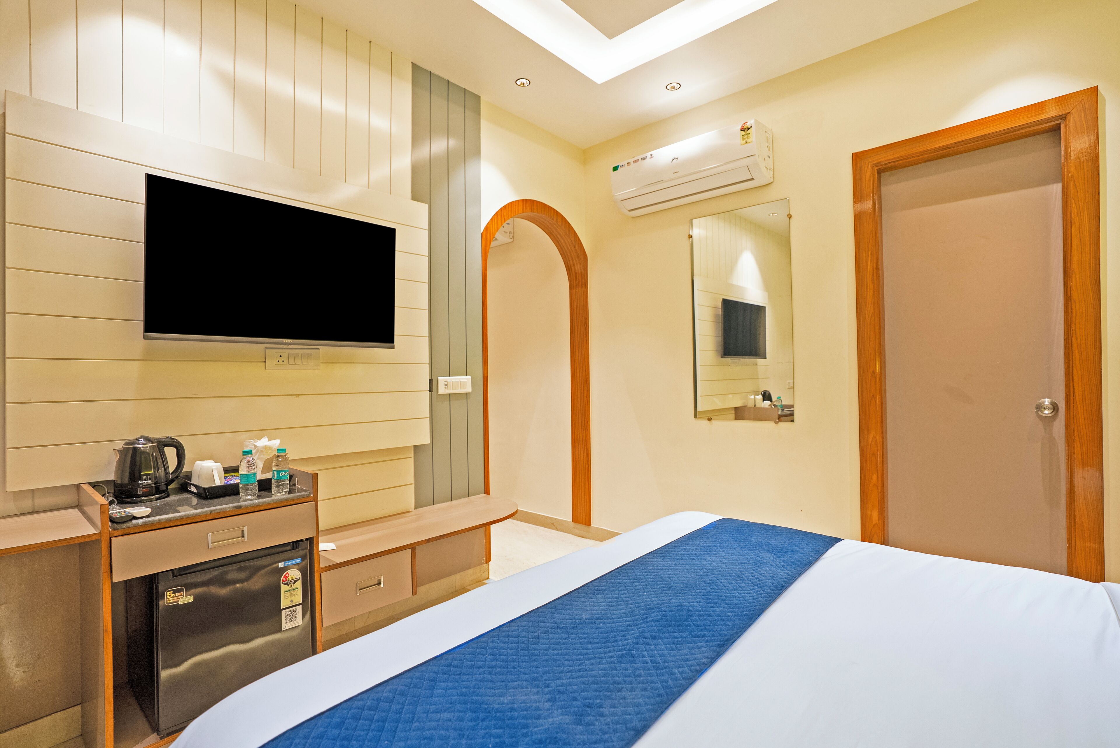 Une chambre d’hôtel équipée d’un lit, d’un téléviseur fixé au mur, d’un mini-réfrigérateur, d’une machine à café et d’un miroir.