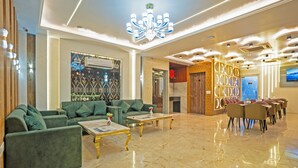 A spacious lobby with green sofas, a chandelier, and a dining area with tables and chairs. - The Prominence Hotel Restaurant & Bar (Greater Noida)