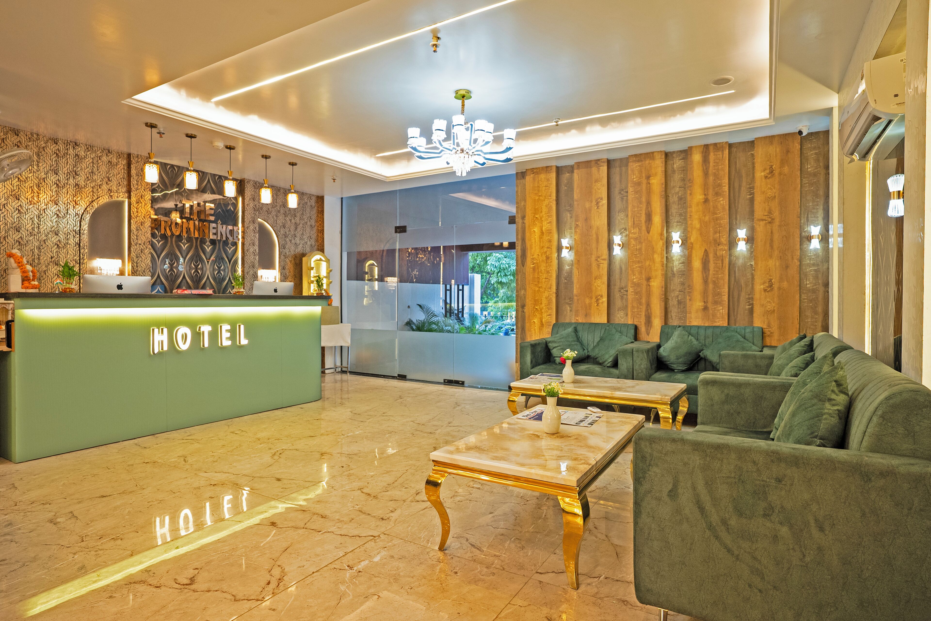 A hotel lobby with a reception desk, green sofas, a marble coffee table, and a chandelier.
