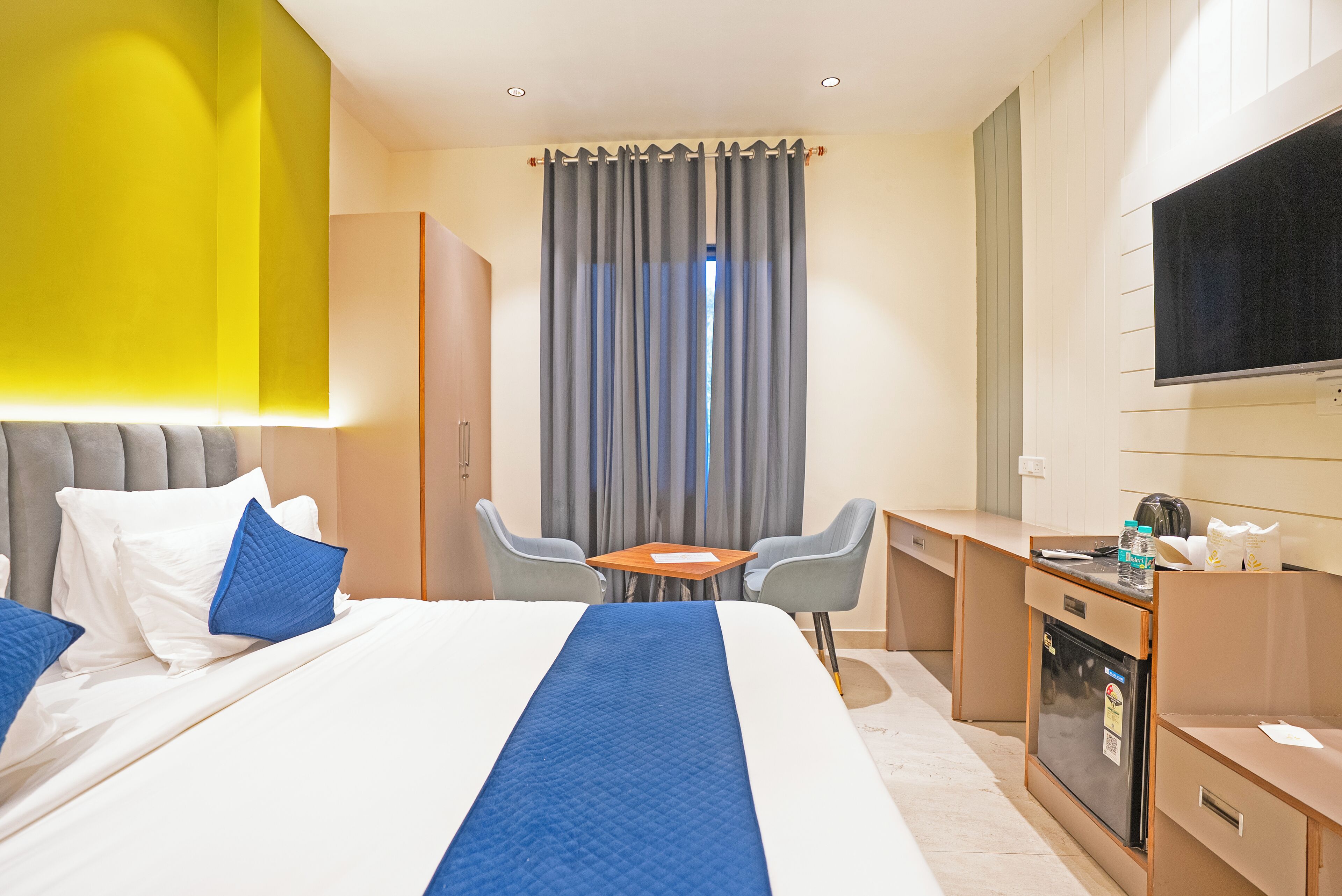 A hotel room with a bed, a desk, a chair, a television, and a minibar.