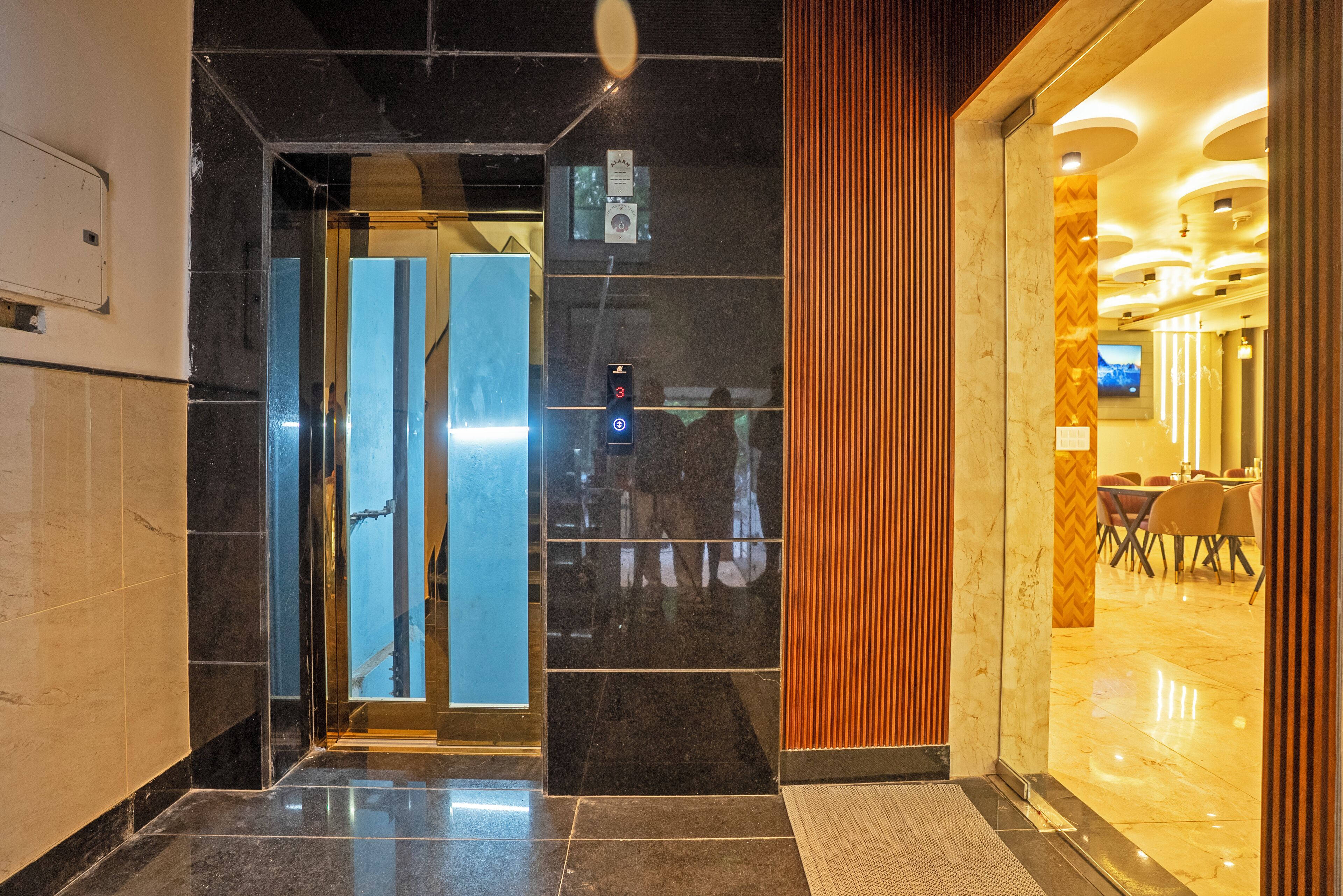 A hotel lobby with a marble floor, a reception desk, and a dining area visible through the glass doors.