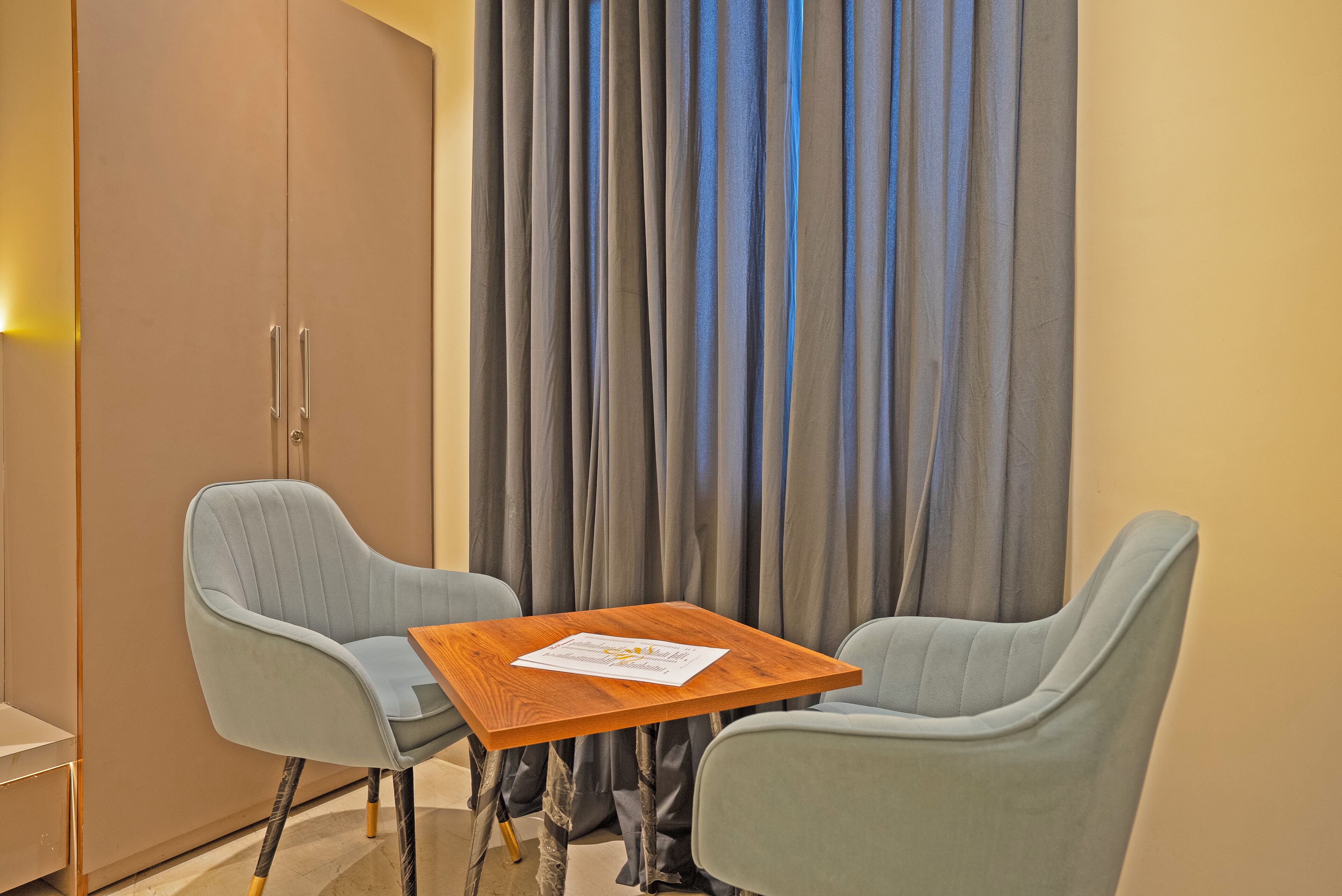 A room with two light blue armchairs, a wooden table, and a large wardrobe.