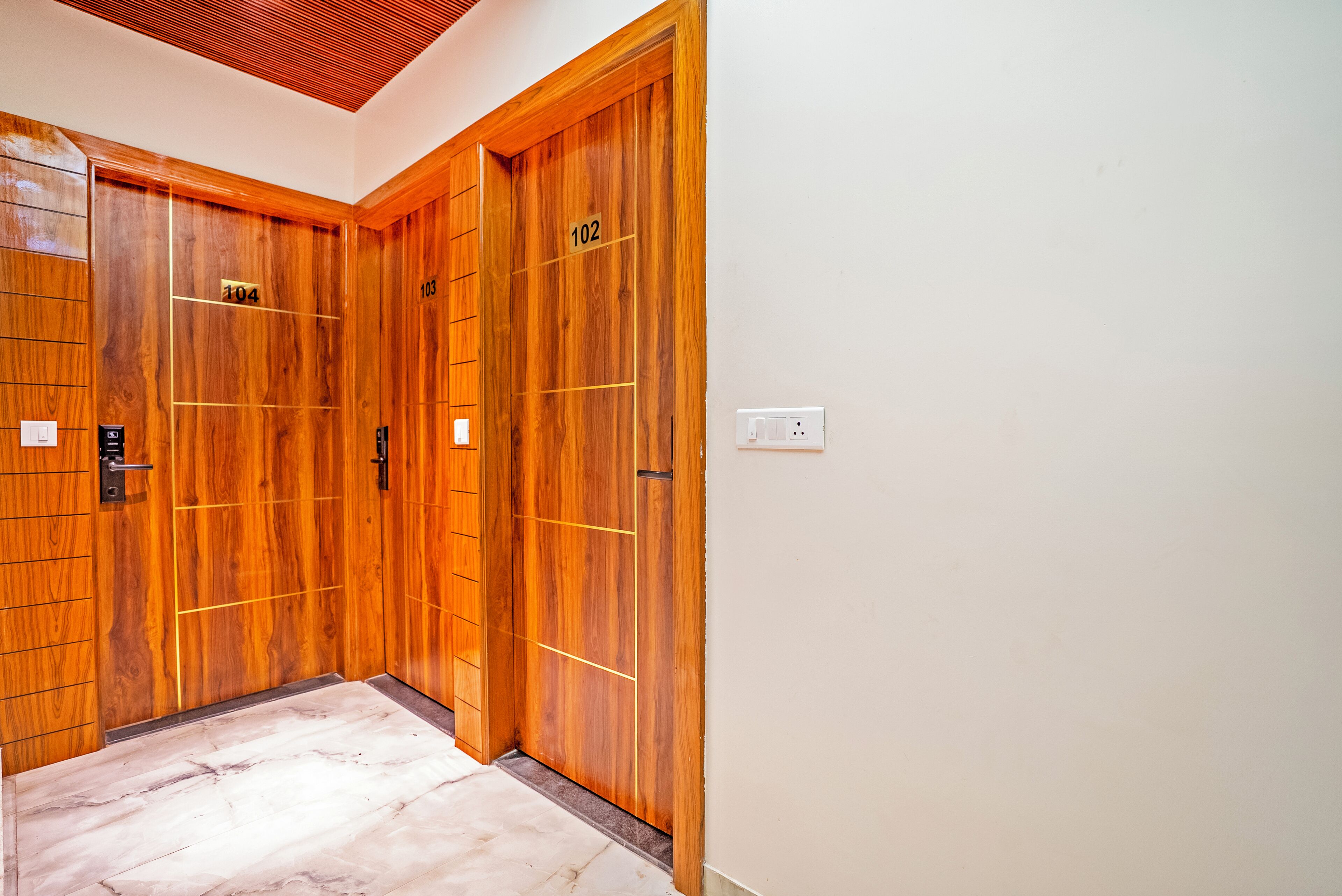 A hallway with wooden doors numbered 102 and 104, a marble floor, and a white wall.