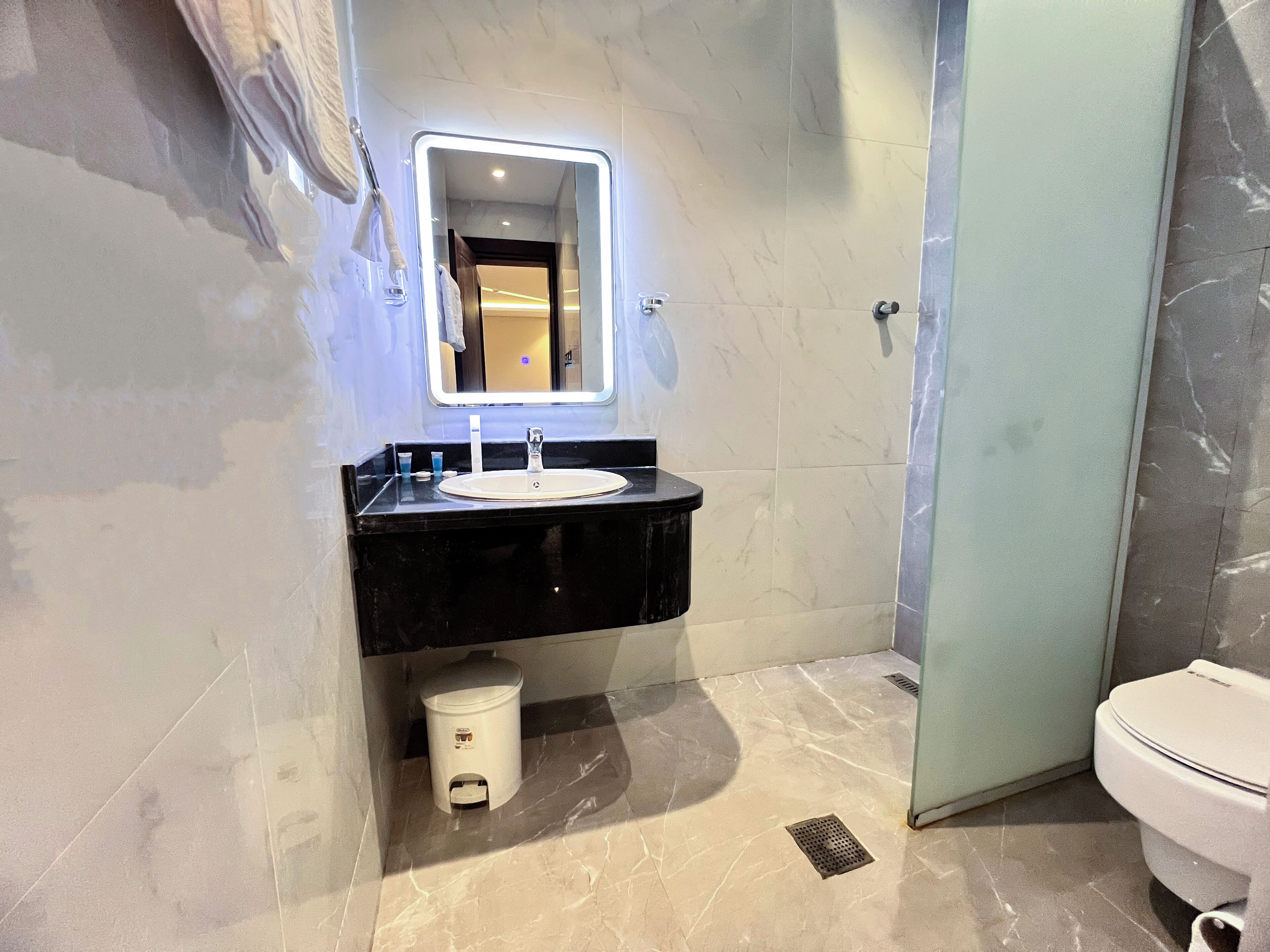 Un baño moderno con un lavabo negro, un espejo con luz, un inodoro y un cesto de basura.