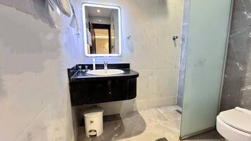 Un baño moderno con un lavabo negro, un espejo con luz, un inodoro y un cesto de basura.