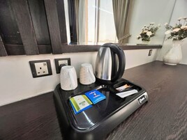 Cocina americana en una habitación de hotel, con cafetera, dos tazas, una bandeja con una tarjeta y un pequeño paquete, y un enchufe.