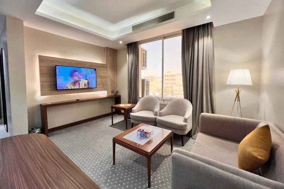 Una camera d'albergo con una TV a schermo piatto montata a parete, due divani, un tavolino da caffè e una lampada.