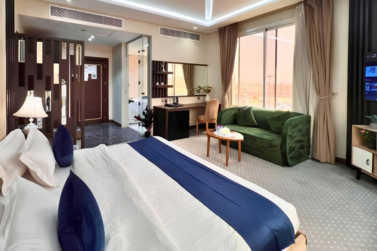 A hotel room with a bed, a desk, a green sofa, and a view of the city.
