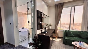 A modern living room with a glass partition, a sofa, a coffee table, and a view of the city. - AL Ewan Pro Serviced Apartments (Al Kharj)