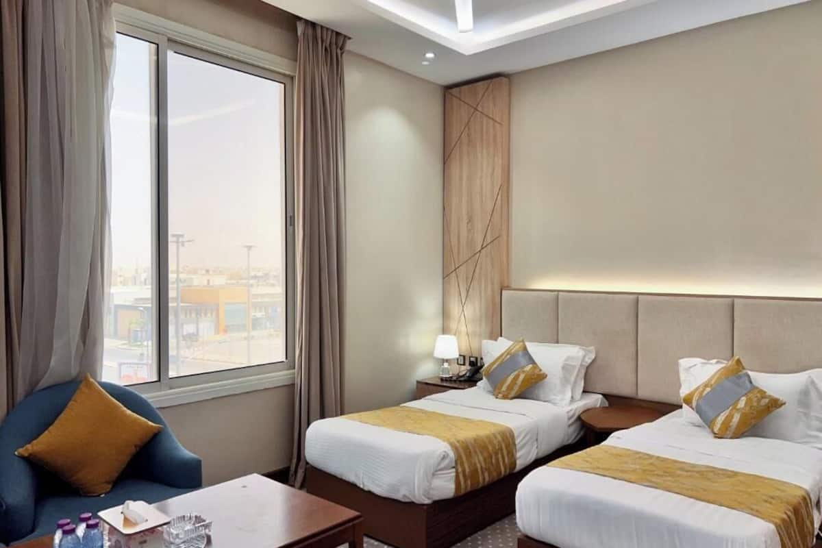 A hotel room with two beds, a desk, a chair, a window with curtains, and a view of the cityscape.