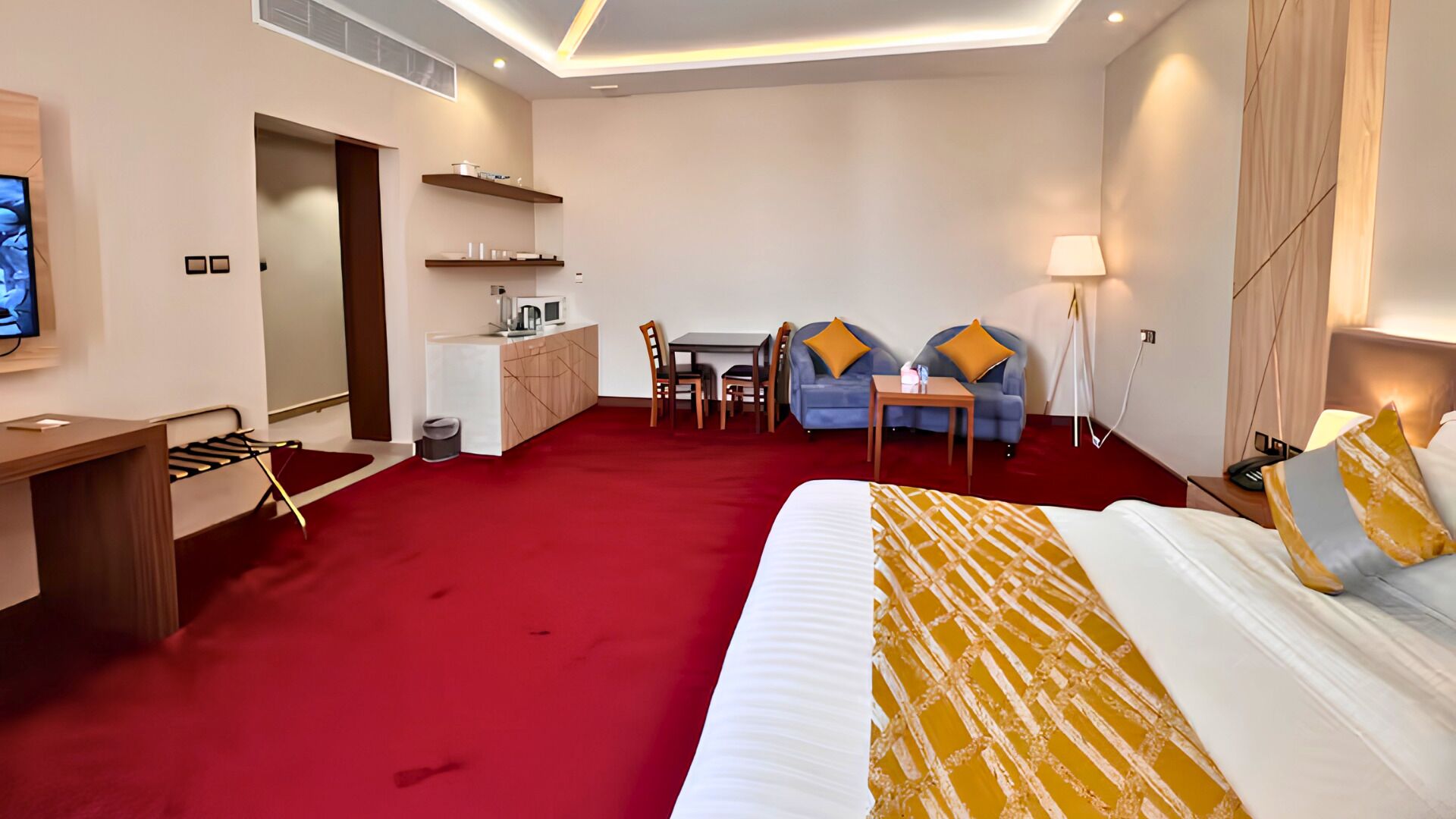 Una habitación de hotel con cama, escritorio, kitchenette, comedor y zona de estar.