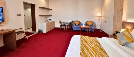 Una habitación de hotel con cama, escritorio, kitchenette, comedor y zona de estar.