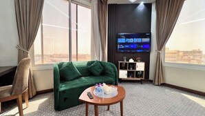 A modern hotel room with a green sofa, a wooden coffee table, and a flat-screen TV displaying a smart TV interface. - AL Ewan Pro Serviced Apartments (Al Kharj)