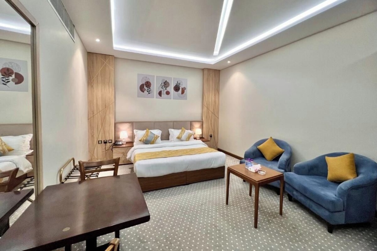 A hotel room with a bed, a sofa, a table, and artwork on the wall.
