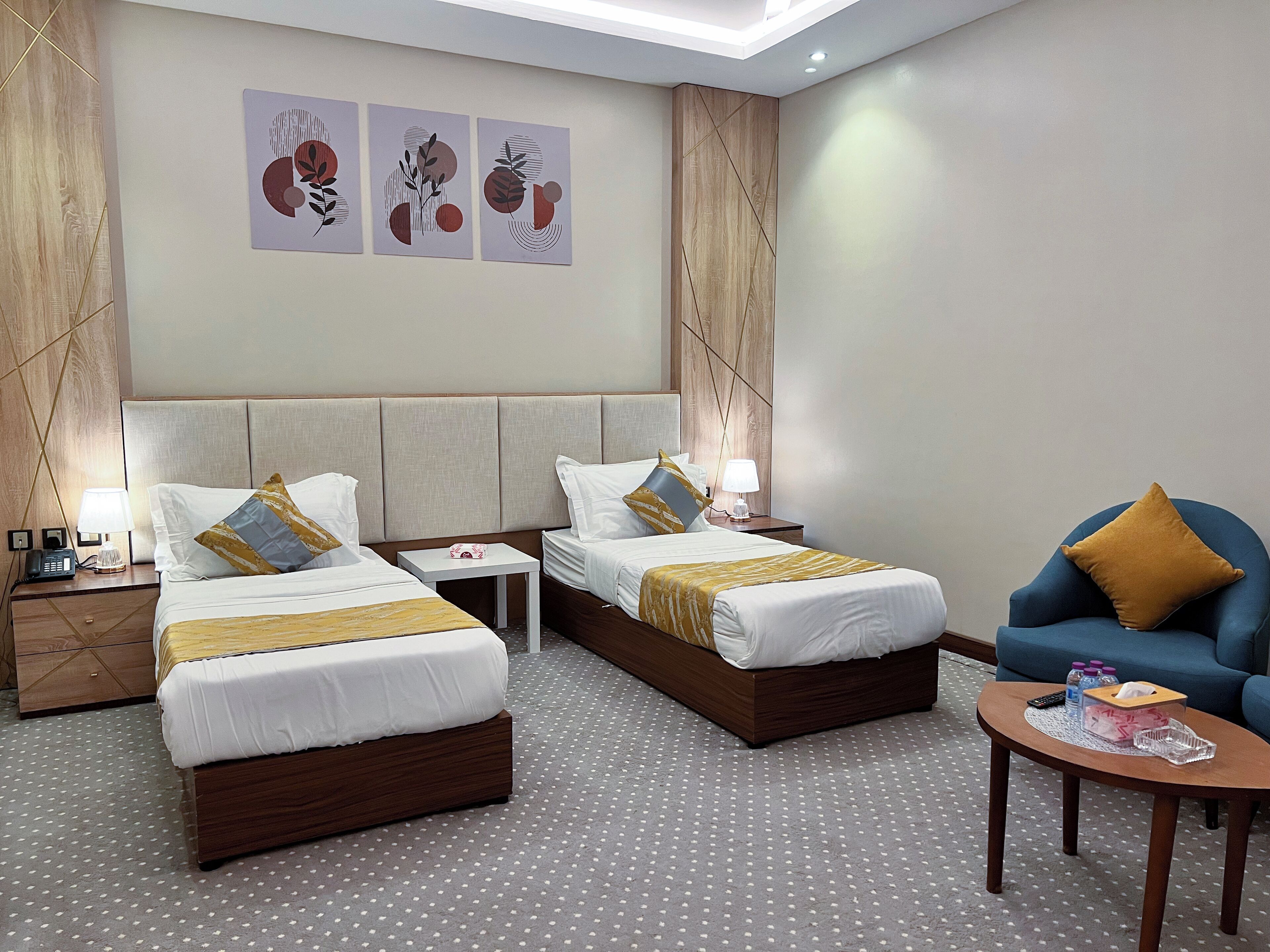 A hotel room with two beds, a small table, a chair, and artwork on the wall.