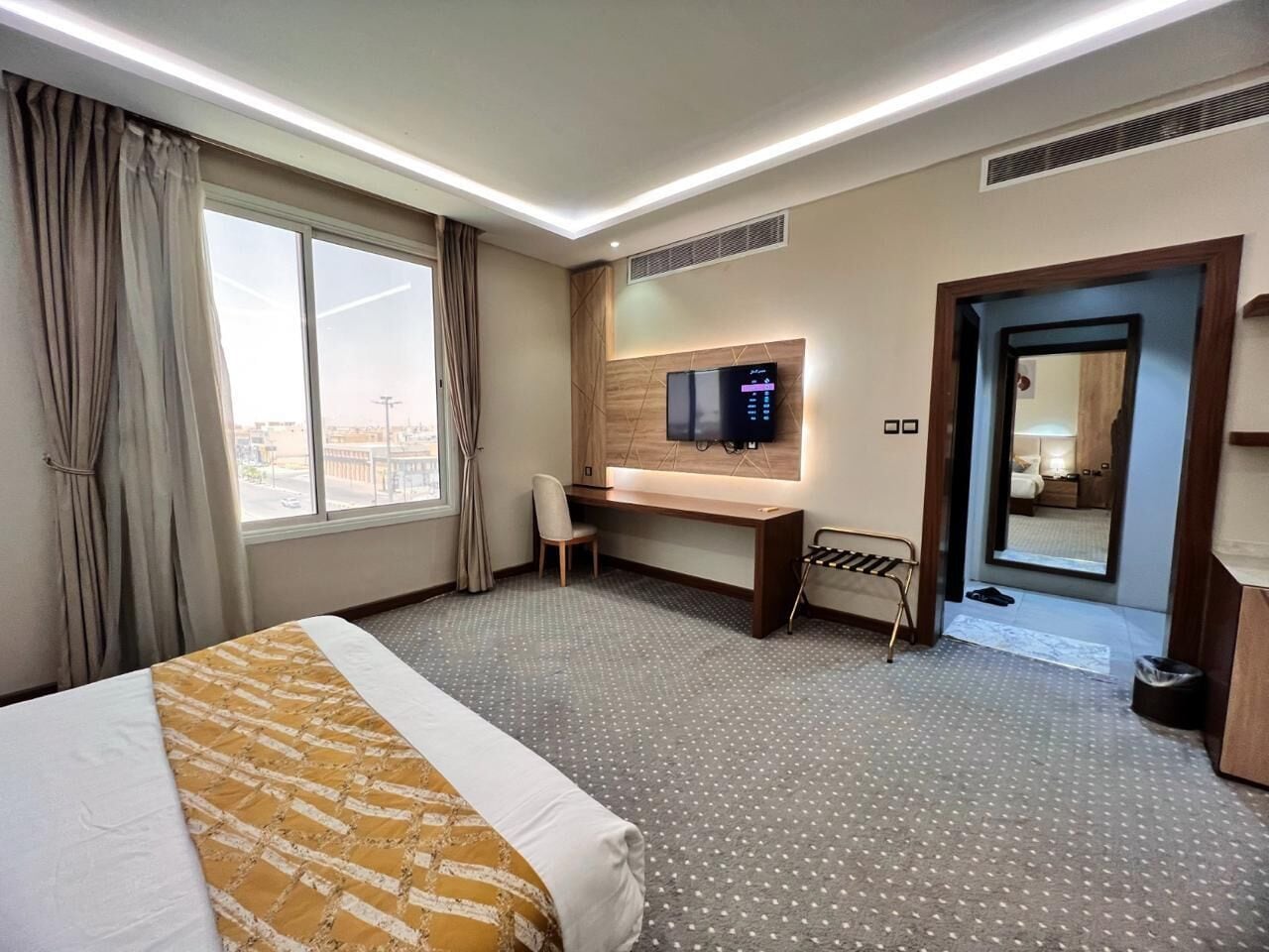 A hotel room with a bed, a desk, a television, and a view of the city through the window.