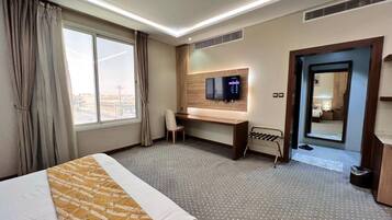 A hotel room with a bed, a desk, a television, and a view of the city through the window.