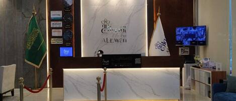 A hotel reception area with a marble counter, a flag, a reception desk, a television, and a blue sofa.