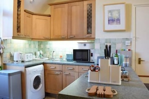 A kitchen with wooden cabinets, a microwave, a washing machine, and a countertop with various items.