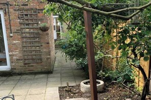 Un bâtiment en briques avec un patio carrelé, une plante suspendue et un pot de fleurs fait à partir d’un pneu.