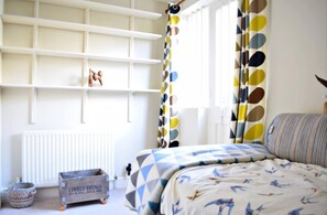 Um quarto com uma cama, um radiador, uma caixa de armazenamento pequena e uma janela com cortinas.