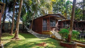 A small wooden building with a porch, surrounded by palm trees and a hammock. - Swarg Resort (Mawal)