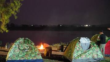 Two camouflaged tents set up near a lake with a campfire between them.