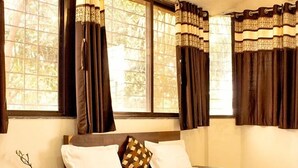 A bedroom with a bed, nightstand, and window with curtains. - Swarg Resort (Mawal)