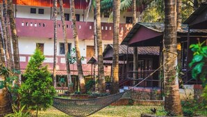 A multi-story building with a red and white facade, surrounded by palm trees and a hammock in the foreground. - Swarg Resort (Mawal)
