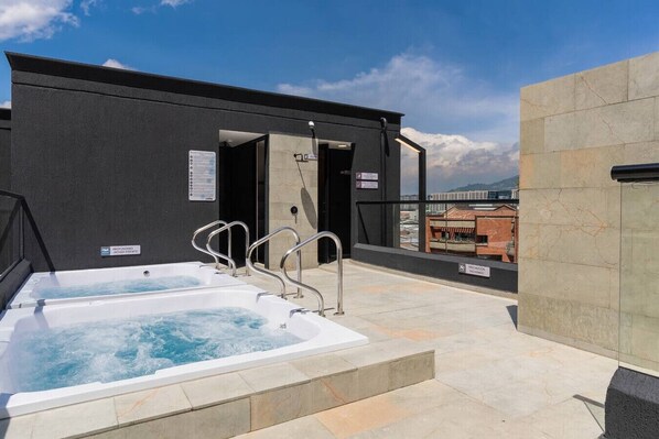 Un espace spa aménagé sur le toit, comprenant deux bains à remous et une entrée avec une porte en verre.