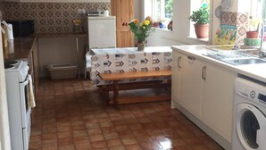 A kitchen with a washing machine, a wooden table, and a window with a flower pot. - Comfy Holiday Home & Beach Hut (Sutton on Sea)