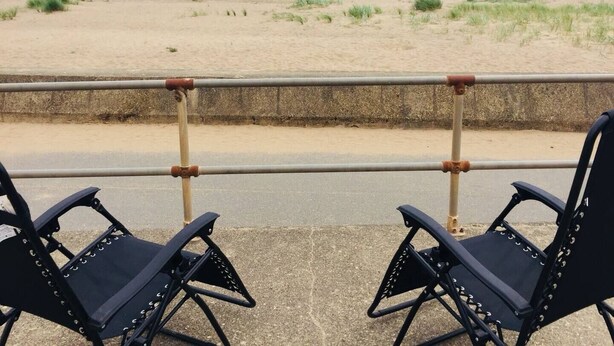 Two black chairs with metal frames and rivets, positioned on a concrete surface with a metal railing in the foreground. - Comfy Holiday Home & Beach Hut (Sutton on Sea)