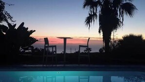 A poolside area with two chairs and a table, surrounded by palm trees and a sunset view. - Exclusive Golf Villa (Private Swimming Pool) Costa Adeje (Adeje)