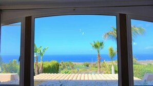 A room with large windows offering a view of the ocean and palm trees. - Exclusive Golf Villa (Private Swimming Pool) Costa Adeje (Adeje)