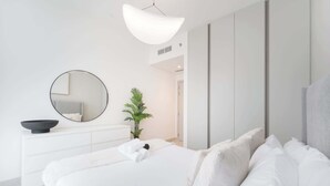 A modern bedroom with a large bed, a round mirror, a small plant, and a white dresser.