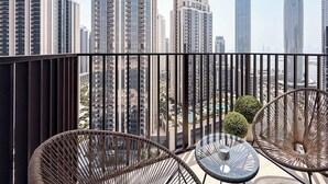 A balcony with wicker chairs and a small table, overlooking a cityscape with high-rise buildings.