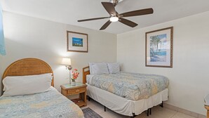 A bedroom with two beds, a ceiling fan, a nightstand with a lamp, and framed pictures on the wall.