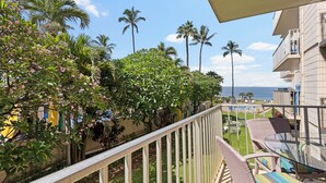 A balcony with a view of the ocean, palm trees, and a pool area.