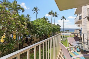 A balcony with a view of the ocean, palm trees, and a pool area.