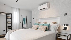 Une chambre à coucher moderne avec un grand lit, un appareil de climatisation, une table de chevet avec une lampe et une échelle appuyée contre le mur.