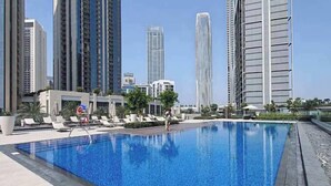 A swimming pool with lounge chairs and a lifeguard stand, surrounded by high-rise buildings.