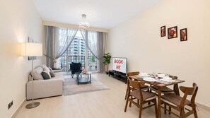 Un salon moderne avec un canapé, une table à manger dressée pour quatre personnes, un téléviseur et un panneau indiquant : « Réservez-moi ».