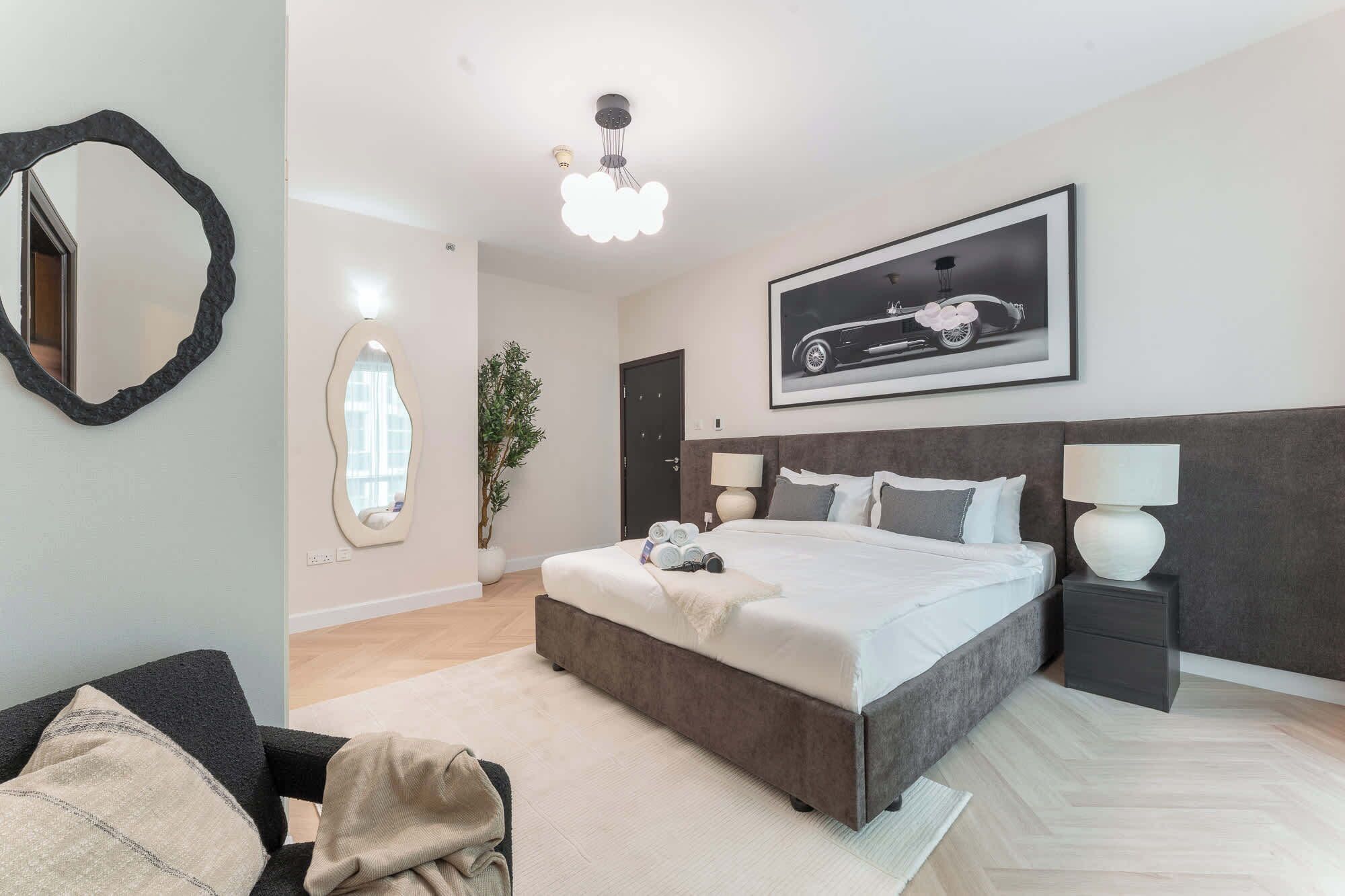 Une chambre à coucher moderne avec un grand lit, une tête de lit, des tables de chevet, un miroir et un tableau encadré au mur.