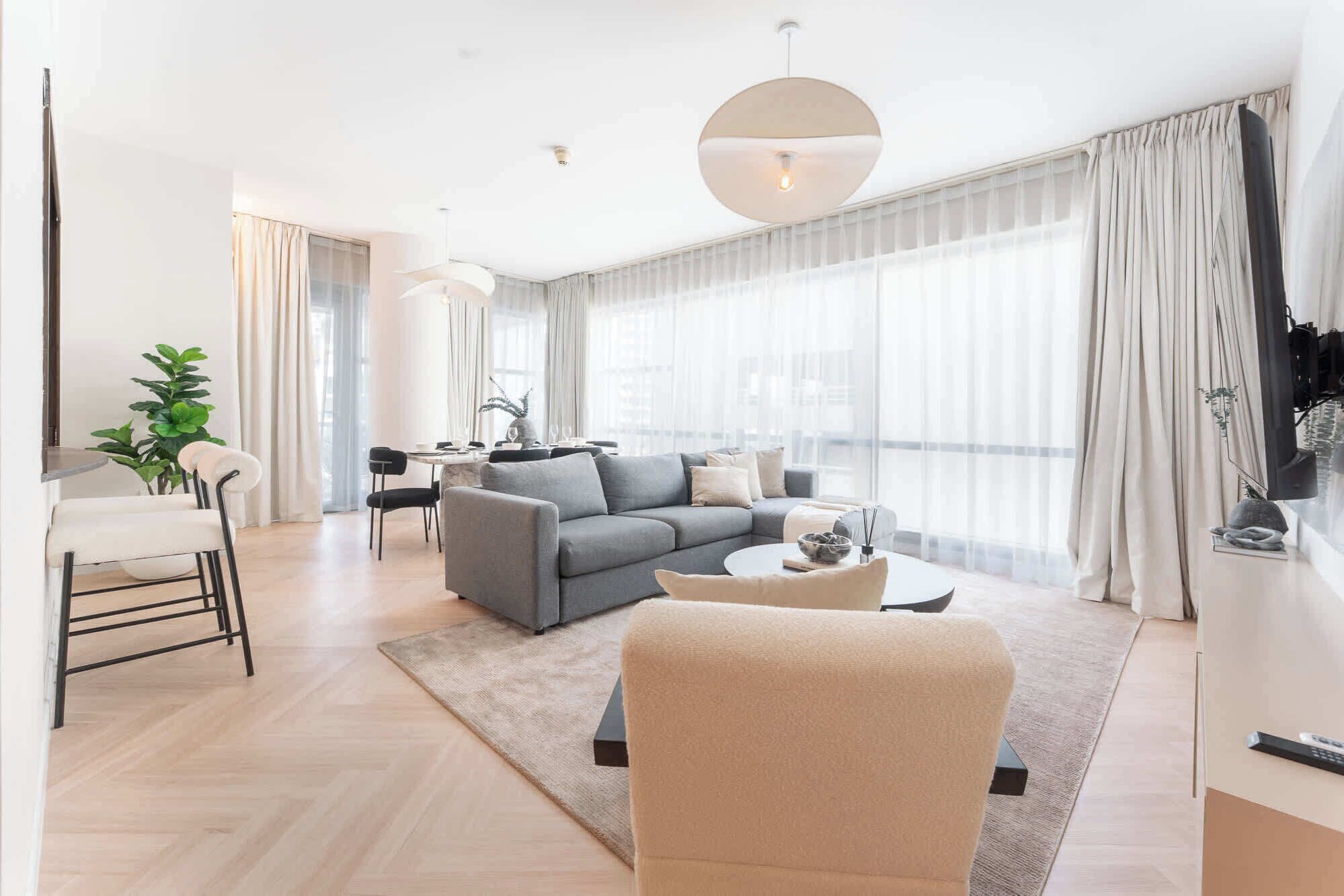 A modern living room with a grey sofa, a beige armchair, and a dining area with a table and chairs.