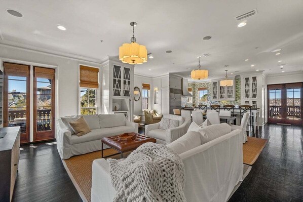 A spacious living room with white sofas, a coffee table, and a large window.