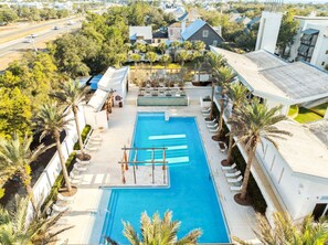 A swimming pool with sun loungers, palm trees, and a view of a residential area.