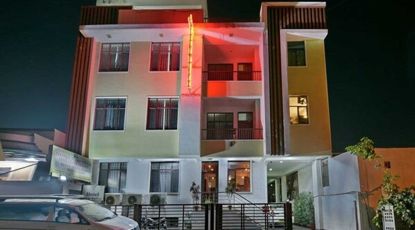 A multi-story hotel with a central staircase, air conditioning units, and a gated entrance.