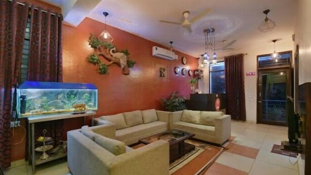 A living room with a sectional sofa, a fish tank, and a ceiling fan. - Hotel O Hari Villa (Jaipur)