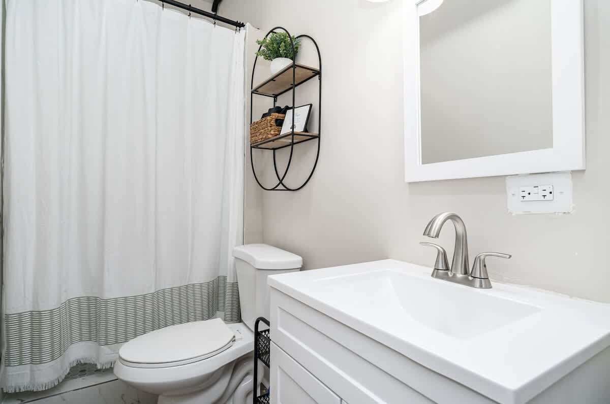 A bathroom with a white sink, a toilet, a shower curtain, and a wall-mounted shelf with a plant.